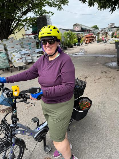 Person standing with a bike with flowers in baskets & a garden center in the background