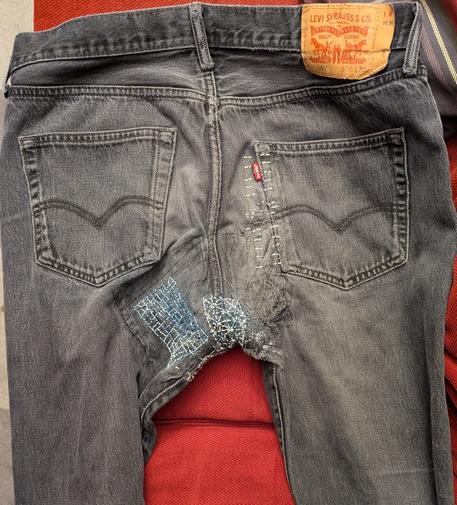The back of a pair of charcoal jeans with some sashiko-style patches on them where rips have formed. There is some blue water-soluble marker staining where I drew a grid on the fabric to aid with the sashiko