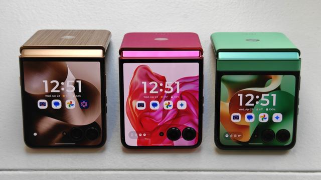 Photo of Moto's 2025 Razr Ultra (left, wood brown), Razr+ (middle, hot pink), and Razr (right, apple green) lineup propped in a line on a white surface in "tent' mode.
