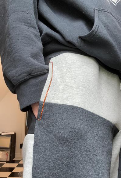 Me wearing color-blocked sweatpants, with my hand in the pocket, showing the orange and black stitch details.