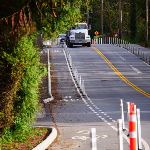 Riverside Dr at Old Dollarton Rd looking north. There is a bike lane on each side of the road, separated from cars by flex-posts.