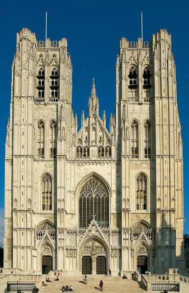 The image features the front facade of a large Gothic cathedral characterized by its two tall towers, intricate stonework, and elaborate architectural details. The structure likely has pointed arches and decorative elements typical of Gothic architecture, set against a clear blue sky. The scene also includes people at the base of the cathedral, suggesting it's a public space.

Image Credits: Wikimedia / Luc Viatour / CC BY-SA 3.0