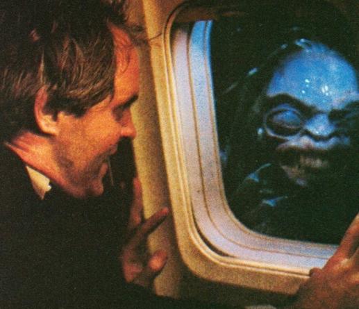 A still from the Twilight Zone movie of stressed out John Lithgow sitting in an airplane and looking out the window. A creature is smirking at him.