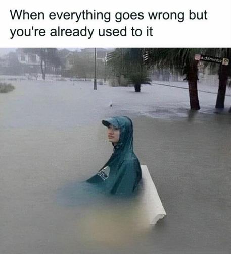 A young person wearing a raincoat and sitting on a bench which seems to be nearby a road with water covered up to the elbow. The scene looks like aftermath of heavy rain which covered entire area. On top of the image "when everything goes wrong but you're already used to it" is written.