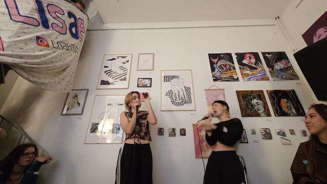 Die feministische Band Lisae rappt vor Kunstwerken, die die Wand schmücken.