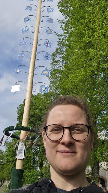 Ein Foto von mir vor dem Maibaum. Im Hintergrund Bäume und etwas blauer Himmel.