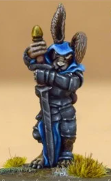 We have an anthropomorphic hare warrior with dark grey fur. He has a blue hood and cloak over dark silver chainmail armour. He's holding a large two-handed sword that's as tall as he is with its pommel up and the blade on the ground.