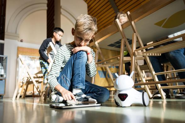 Eine Junge sitzt auf dem Boden und programmiert einen Roboter mit dem Tablet.