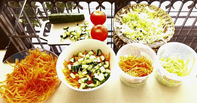 Shredded Lettuce, grated carots, diced cucumbers being sorted into a bowl and containers with tomatoes to be diced and a quartered orange to be added later. Dinner prep for the next few days.