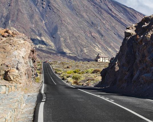 una strada che si perde in un deserto di pietre con una parete rocciosa sullo sfondo.