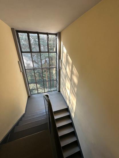 A view from the top of a stairwell of a mezzanine landing. A large window fills the opposing wall.