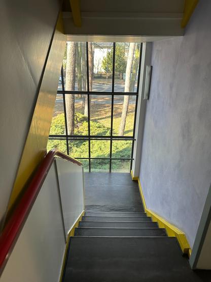 A view down a stairwell towards a large window. Sunlight reflects off the light yellow paint on the stairs