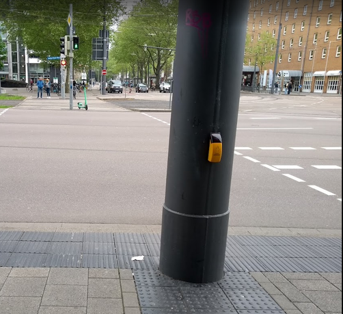 Mendelsohnplatz in Karlsruhe: Blick vom Röserhaus Richtng Scheck-In.
Im Vordergrund massiver Ampel-/Oberleitungsmast mit Bettelampel direkt auf Blindenleitstreifen, Im Hintergrund auf Mittelinsel und Gegenseite erkennbar gleiche Anordnung der dortigen Masten.