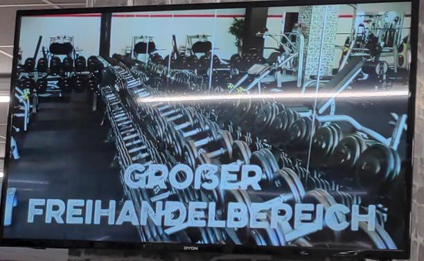 Bild aus einem Fitnesscenterwerbevideo. Ein Raum mit vielen Hanteln. Darunter steht "GROẞER FREIHANDELBEREICH"