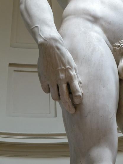 Detail einer weißen Marmorstatue ( Michelangelos David) zeigt eine männliche Hand, die an einem Oberschenkel anliegt