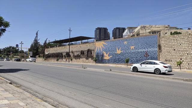 A road with an artwork showing the sun and four flying birds at a wall.