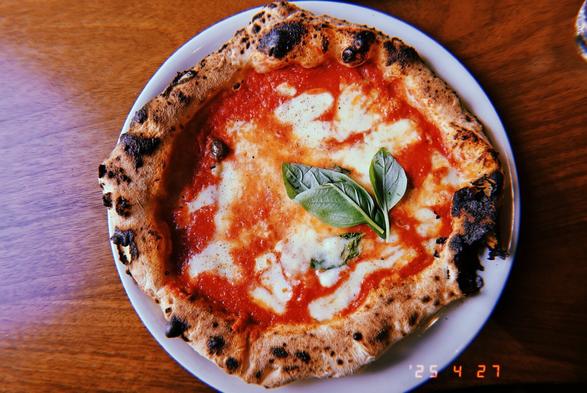 A whole Napoli-style pizza on a plate garnished with two leaves of basil pictured from a bird's-eye view.