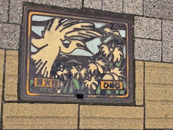 Manhole cover showing storks or cranes flying over flowers