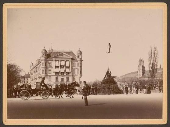 Ein historisches Bild zeigt das Sächsilüüte von 1892.
Auf einem Platz ein grosser Haufen, aus dem ein Masten ragt. Darauf ein Böögg. Drumherum eine Person in Uniform, eine Kutsche und einige Zuschauerïnnen.