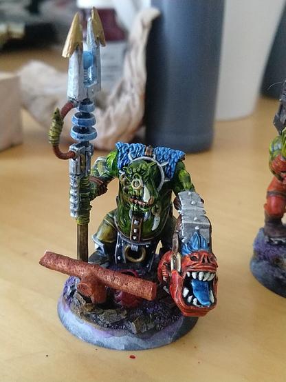 A big ork with a zappy stick and a squig on a leash, the base covered in rusty garbage and other stuff.