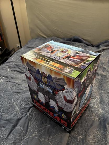 Illustrated box for Haslab Transformers Omega Prime. The top shows Omega Prime’s head and chest, while the front shows him in a more athletic flexing pose. The right side of the box shows Ultra Magnus from the waist up.