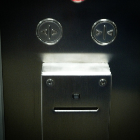 Passcard-reader elevator control, whose card slot, screws, and indicator light form a tiny robotic face.