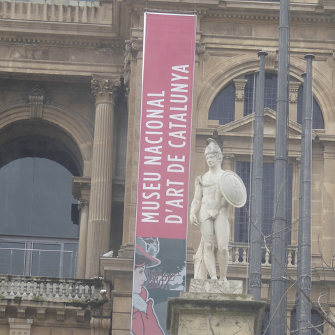 Banner reading Museu Nacional d'Art de Catalunya in front of a classical building facade, and flanked with a statue of a warrior.