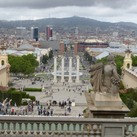 A plaza as seen from the top of its grand stairs, with pillars, fountain, and venetian-inspired towers in the distance.