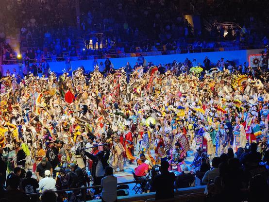 This photo is towards the end of grand entry on Day 1. There are so many dancers in the coliseum that the floor can no longer be seen. The dancers are wearing regalia that represented not only the dance they were going to compete in, but also their families and tribal affiliations. You really cannot make out too much individualization among the mass of people on the floor. Needless to say there are tons of feather, beads, sequins and fringes being worn. There has to be thousands of dancers on the floor.
