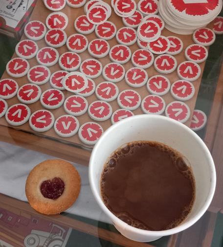 En syltkaka där sylten har formen av ett hjärta. En kopp kaffe med mjölk och en karta med V-magneter