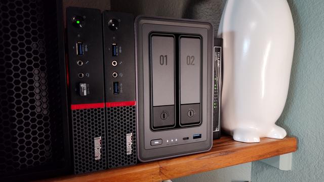 A Ugreen 2800 NAS to the right of a pair of Lenovo m900 Tiny PCs sitting on a shelf.