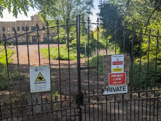 An image of a gate with signs from the British Transport Police saying that the area is private land and police dogs were in training 24 hours a day

A building can be seen in the background, it is boarded up