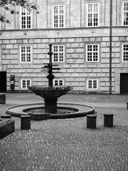 Black and white photo of a fountain in a public square. There is some noticable motion blur from camera movement.