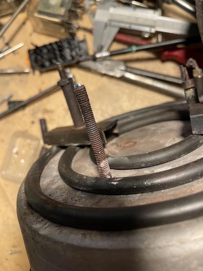 Eine der Gewindestangen von der Seite gesehen. Hitze und Feuchtigkeit haben das Gewinde sichtbar angegriffen. Ich möchte diese Stangen nach möglichkeit erhalten da die Verbindung zum Aluminium des Topfes so aussieht als sei die Stange darin fest vergossen
