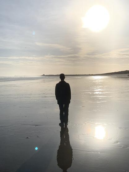 Figure silhouetted against sun on beach