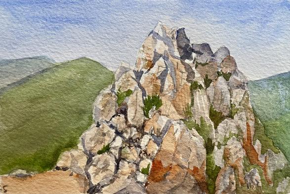 A jagged, craggy rock formation rises sharply from a gentle landscape of smooth, rolling hills, with small patches of plants clinging to its cracks and ledges under an open, clear sky.