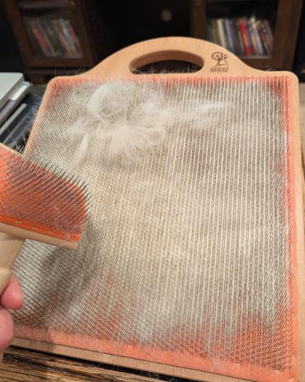 A blending board partly covered in white fluff has a light clump of white husky underfur near the top, waiting to be combed in by the blending brush held off to the side.