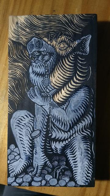 Un trozo de madera, pintado de negro, con un dibujo en tinta blanca parcialmente tallado.