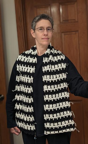 me in front of a white wall and brown wooden door, in navy pajamas, wearing the cat scarf draped over my shoulders with the two ends hanging down in front