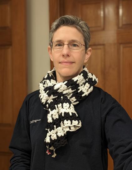 me in front of a brown wooden door, wearing navy pajamas, with the cat scarf wrapped around my neck in a girth hitch and two short ends making a sort of jabot in front