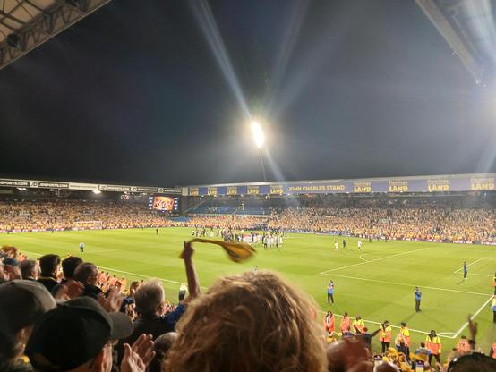 Elland road celebrating Leeds united being promoted. Fans are wearing yellow and waving their scarves. The players and coaching staff are on the pitch.