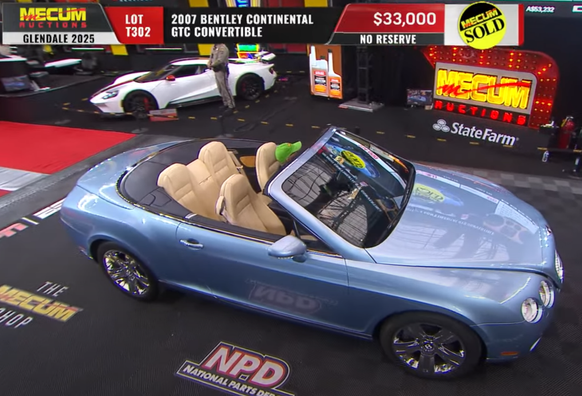 Bentley Continental GTC convertible in pale blue with tan interior, leaving the auction block after selling at no reserve for $33K at Mecum Auto Auctions in Glendale AZ.