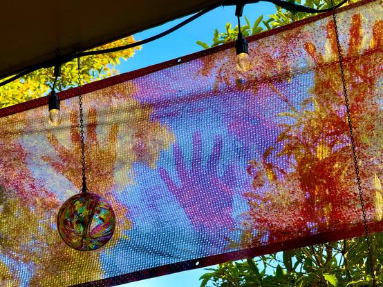 colorful photo of a translucent banner with rock art hands in front of a deep blue sky with foliage