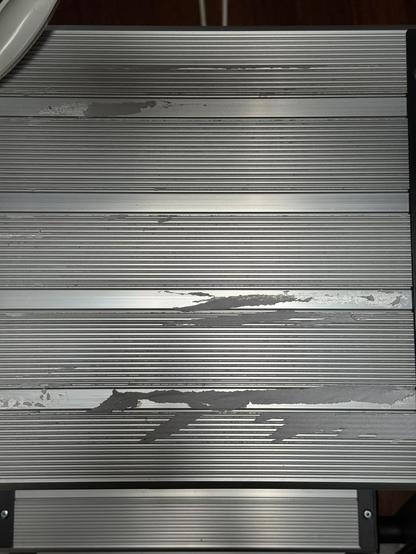 The non-slip surface of the top step of a step ladder, with bits of paper stuck over some of the non-slip area and also between non-slip areas. Not visible: the whole step is sticky from where the sticker was, and needed to be cleaned with methylated spirits.