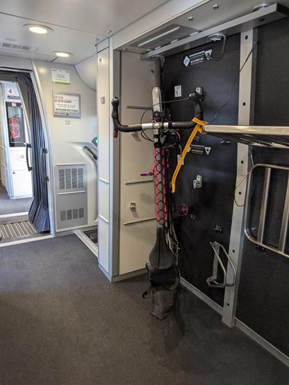 a bicycle hanging from a hook in a train car, strapped to a luggage rack