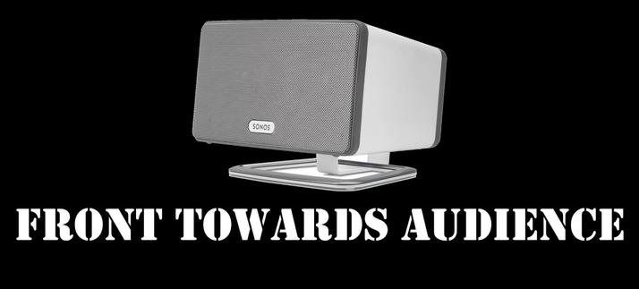 Image of a Sonos Play:3 speaker mounted on a stand, looking like a claymore mine, with the text "FRONT TOWARDS AUDIENCE" in bold white letters against a black background.