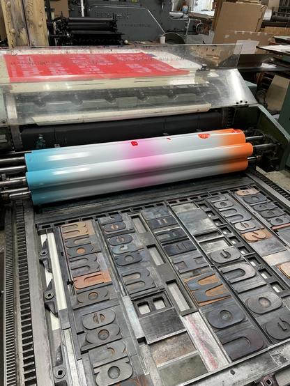 Handsatz mit Holzlettern auf einer Andruckpresse für den Druck eines Plakats. Dritten Druckgang mit Farbverlauf Orange-weiß-Pink-Weiß-Türkis