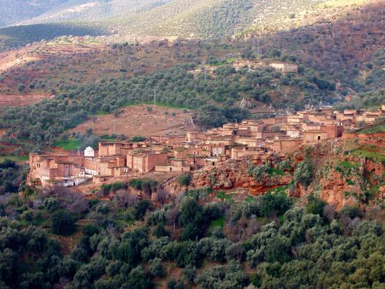 Moroccan village nestled among a red-earth and green landscape of rolling hills and ravines