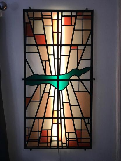 An abstract stauned glass panel suggestive of a sunrise over a lake with mountains, it has symmetry and asymmetry at the same time.