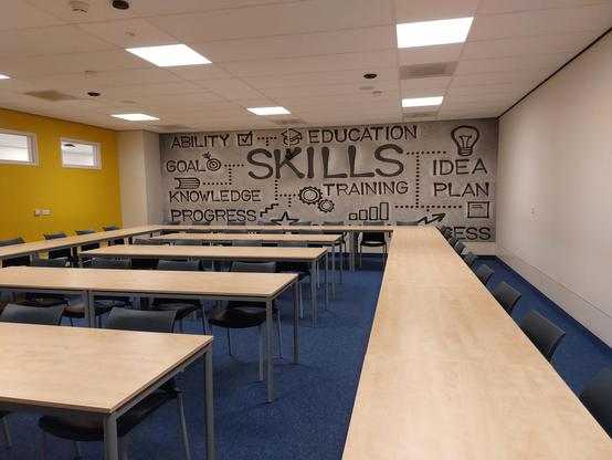 Modern classroom with U-shaped tables, mural with educational keywords on the back wall.